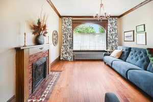 Living room featuring ornamental molding, radiator, a chandelier, hardwood / wood-style floors, and a brick fireplace