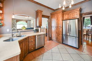 Kitchen featuring a chandelier, stainless steel appliances, brown cabinetry, arched walkways, and crown molding