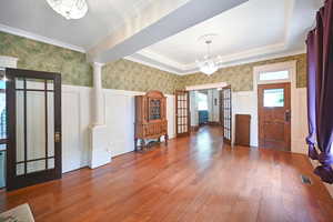 Entrance foyer with wallpapered walls, a chandelier, a decorative wall, plenty of natural light, and wood finished floors