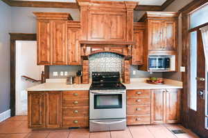 Kitchen featuring stainless steel appliances, light countertops, light tile patterned floors, and brown cabinetry