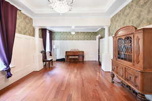 Foyer entrance with decorative columns, a decorative wall, wallpapered walls, wood-type flooring, and wainscoting