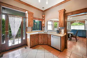 Kitchen featuring stainless steel dishwasher, light countertops, a chandelier, hanging light fixtures, and brown cabinetry