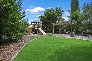 View of grassy yard featuring a pergola, a playground, and a patio