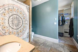 Full bathroom with vanity, stone tile floors, a spacious closet, and a shower with curtain