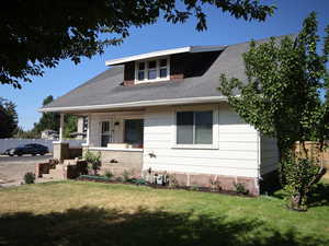 View of front façade featuring a shingled roof, covered porch, and a front yard facing east.