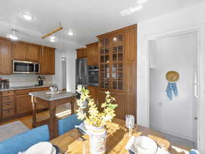 Kitchen featuring backsplash, brown cabinetry, appliances with stainless steel finishes, glass insert cabinets, and a textured ceiling