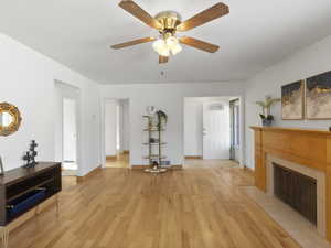 Living room featuring a fireplace with flush hearth, a ceiling fan, and light wood-type flooring