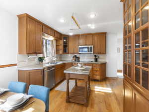 Kitchen with brown cabinets, tasteful backsplash, appliances with stainless steel finishes, light wood-style floors, and glass insert cabinets