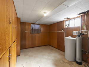 Basement with light floors, a water softener, and wooden walls