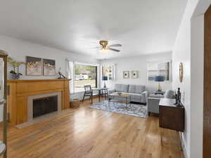 Living room featuring ceiling fan, light wood-type flooring, and a fireplace with flush hearth