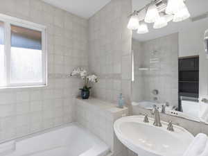 Bathroom featuring a bath, tile walls, and a chandelier