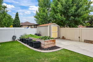 Fenced backyard featuring a shed, a vegetable garden, and a patio area