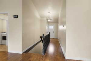 Corridor with wood finished floors, high vaulted ceiling, an upstairs landing, and independent washer and dryer