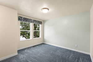 Empty room featuring dark colored carpet and a textured ceiling