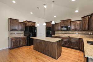 Kitchen with dark brown cabinets, black appliances, a center island, backsplash, and vaulted ceiling