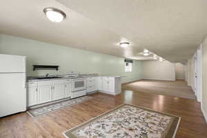 Kitchen featuring white appliances, a textured ceiling, open floor plan, a peninsula, and wood finished floors