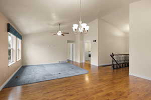 Empty room featuring lofted ceiling, a ceiling fan, a chandelier, and wood finished floors