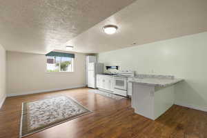 Kitchen featuring white appliances, a peninsula, dark wood-style flooring, a textured ceiling, and white cabinets