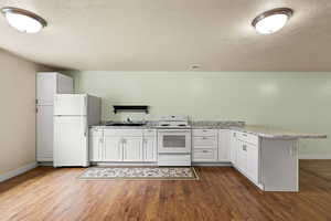 Kitchen with white appliances, a peninsula, dark wood-type flooring, a textured ceiling, and white cabinetry