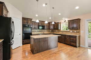 Kitchen with black appliances, dark brown cabinets, backsplash, a center island, and light wood finished floors