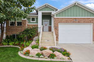 View of front of house featuring board and batten siding, driveway, an attached garage, and brick siding