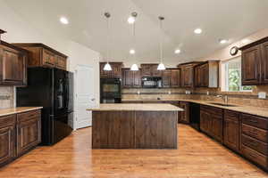 Kitchen with dark brown cabinets, black appliances, a kitchen island, tasteful backsplash, and vaulted ceiling