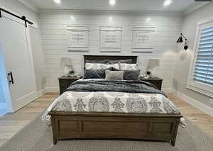 Bedroom with a barn door, light wood finished floors, and ornamental molding