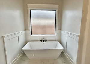 Bathroom with marble finish flooring, a freestanding tub, wainscoting, and a decorative wall