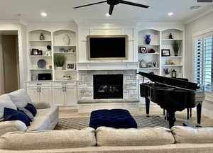 Living room with light wood-type flooring, ceiling fan, crown molding, and a stone fireplace