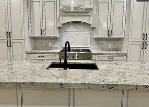 Kitchen with backsplash, light stone countertops, and premium range hood