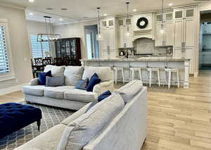 Living room with a chandelier, light wood-style floors, ornamental molding, and recessed lighting