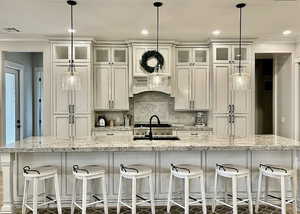 Kitchen with a spacious island, backsplash, light stone countertops, hanging light fixtures, and ornamental molding