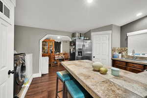 Kitchen with a kitchen bar, stainless steel fridge with ice dispenser, dark wood-style flooring, tasteful backsplash, and separate washer and dryer