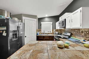 Kitchen featuring appliances with stainless steel finishes, tasteful backsplash, white cabinetry, and tile countertops