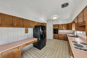 Kitchen with wallpapered walls, black appliances, light floors, light countertops, and brown cabinetry