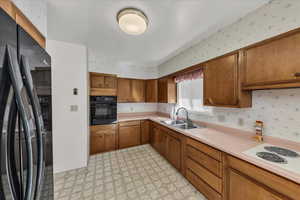 Kitchen with wallpapered walls, black appliances, light flooring, light countertops, and brown cabinets