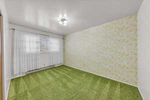 Carpeted empty room featuring wallpapered walls and a baseboard heating unit