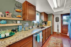 Kitchen with stainless steel dishwasher, light wood-style floors, light stone counters, open shelves, and healthy amount of natural light