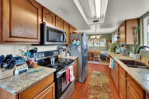 Kitchen with appliances with stainless steel finishes, light wood-style flooring, a chandelier, and brown cabinetry