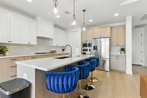 Kitchen featuring stainless steel appliances, tasteful backsplash, a kitchen bar, light countertops, and light wood-style floors