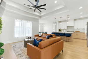 Living area featuring recessed lighting, light wood-style floors, a raised ceiling, a ceiling fan, and a chandelier