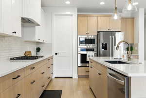 Kitchen with light brown cabinets, stainless steel appliances, light countertops, light wood finished floors, and backsplash