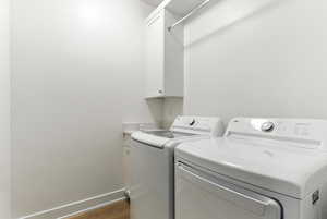 Laundry area featuring washing machine and dryer, cabinet space, and dark wood-style flooring
