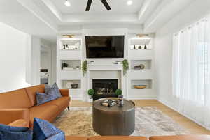 Living area with built in features, ceiling fan, wood finished floors, and a brick fireplace