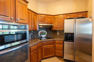 Kitchen with stainless steel appliances, brown cabinets, backsplash, and under cabinet range hood