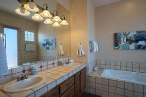 Bathroom with double vanity, a garden tub, backsplash, and a chandelier