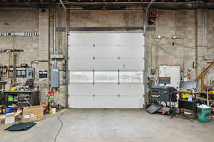 Garage featuring electric panel, a workshop area, and concrete block wall