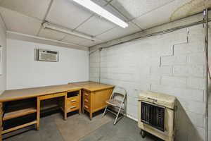 Home office featuring heating unit, a paneled ceiling, concrete block wall, and a wall unit AC