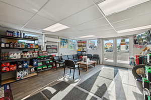 Living area with a paneled ceiling, wood finished floors, french doors, and a wall unit AC