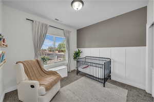Carpeted bedroom featuring a nursery area and wainscoting